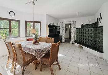 Světlá jídelna, dlažba, krbová kamna, ratanový nábytek, velká okna, moderní design, výhled do zahrady, prostorný pokoj, venkovský styl.