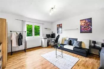 Světlý obývací pokoj s parketovou podlahou, velkými okny a moderními dekoracemi, nabízí pohodlný prostor pro relaxaci i práci.