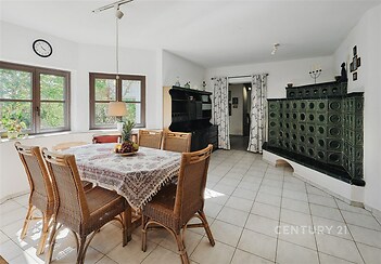 Světlá jídelna, dlažba, krbová kamna, ratanový nábytek, velká okna, moderní design, výhled do zahrady, prostorný pokoj, venkovský styl.
