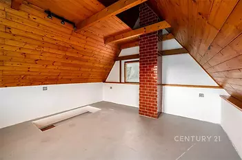 Podkrovní místnost s dřevěným obložením, cihlovým sloupem a velkým oknem, nabízí parketovou podlahu pro moderní útulný styl.