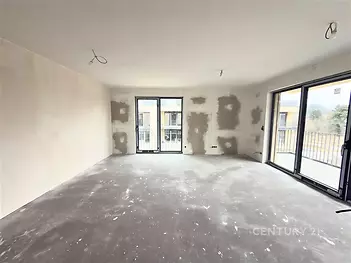 Prostorný obývací pokoj s velkými okny, betonovou podlahou, ideální pro moderní úpravy, skýtá světlý a vzdušný prostor.