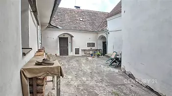 Venkovní dvůr s betonovou podlahou, částečně zastřešený, s rustikálními prvky a zahradním nábytkem, vhodný k rekonstrukci.