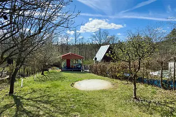 Rozlehlá zahrada s trávníkem a ovocnými stromy, malý dřevěný zahradní domek, klidná lokalita vhodná pro rekreaci.